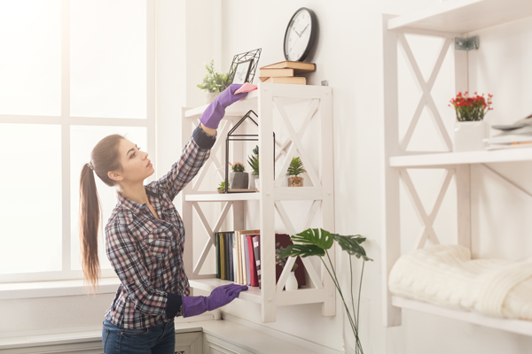 A woman dusting a shelf to improve indoor air quality in her home